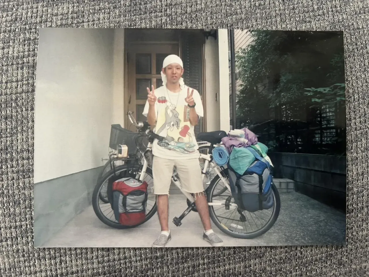 20歳の夏、荷物を積んだ自転車の前でピースサインをする旅の途中の槇野翔太さん